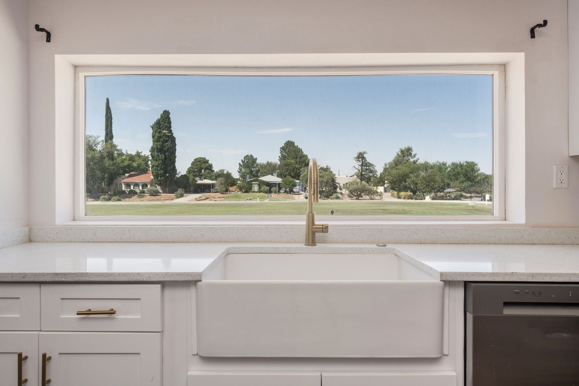 Farmhouse sink and brushed-brass faucet beneath a wide picture window looking out on the city park
