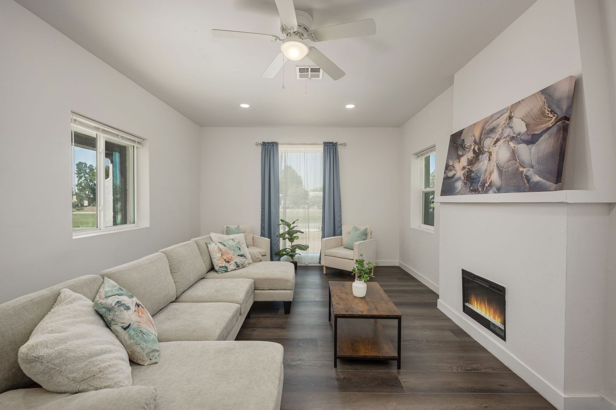 Living room with a fireplace wall, ceiling fan, and wide-plank floors