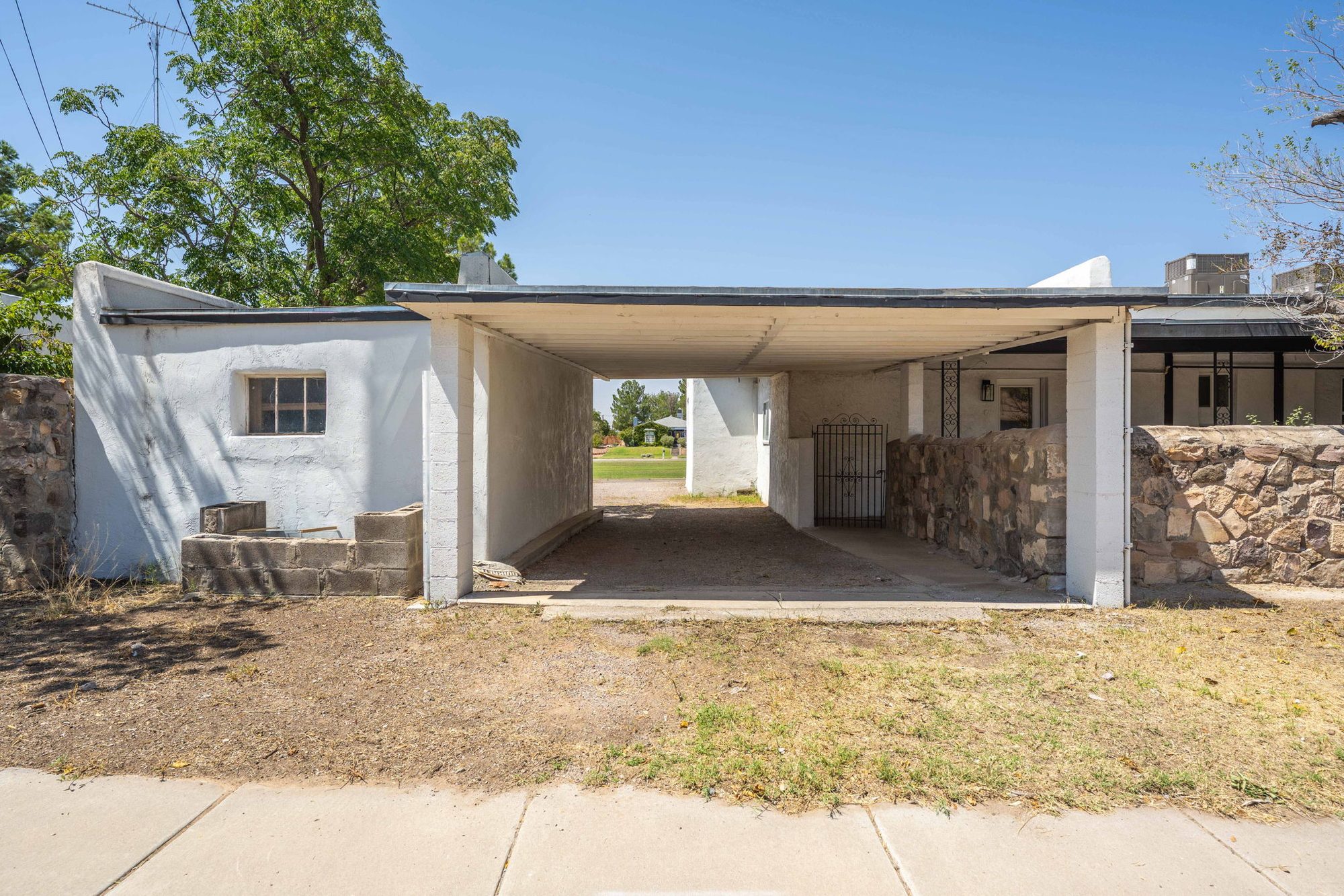 Rear drive-through carport with stone walls and wrought-iron gate