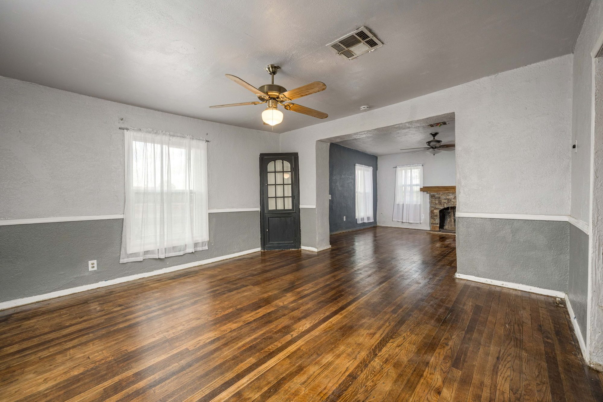 Open living and dining rooms with hardwood floors and an arched glass-paned door