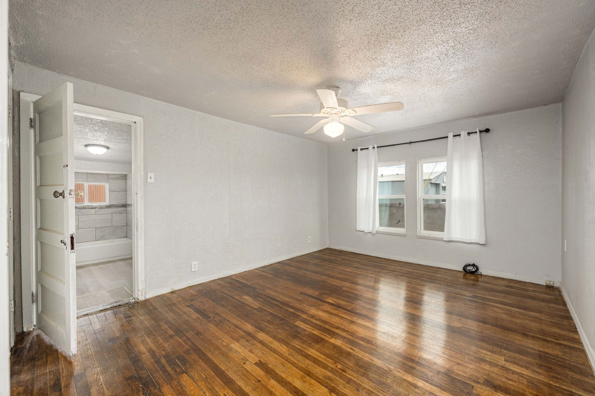 Primary bedroom with hardwood floors and an en-suite bath beyond