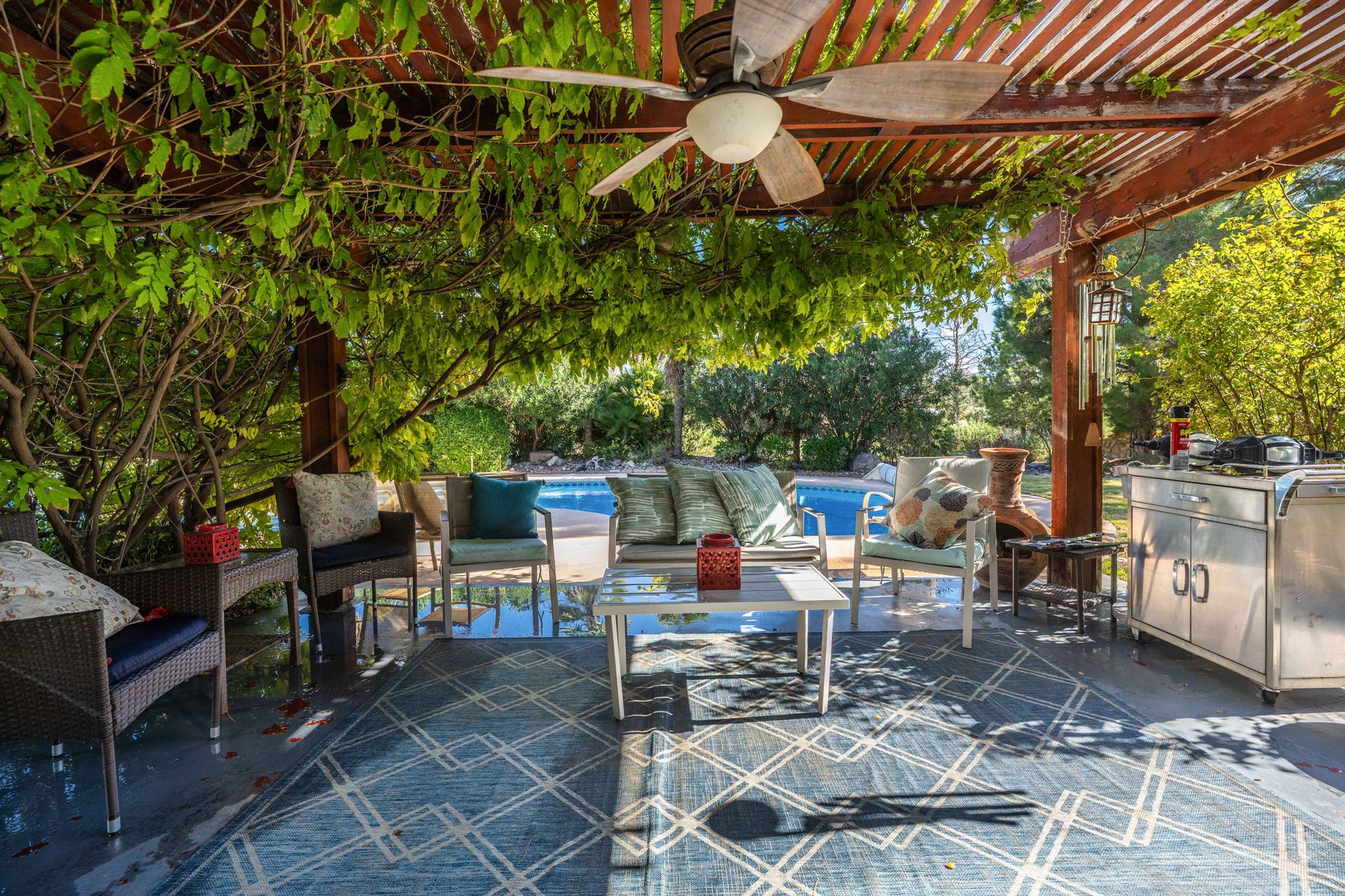 Wisteria-draped pergola with ceiling fan overlooking the pool