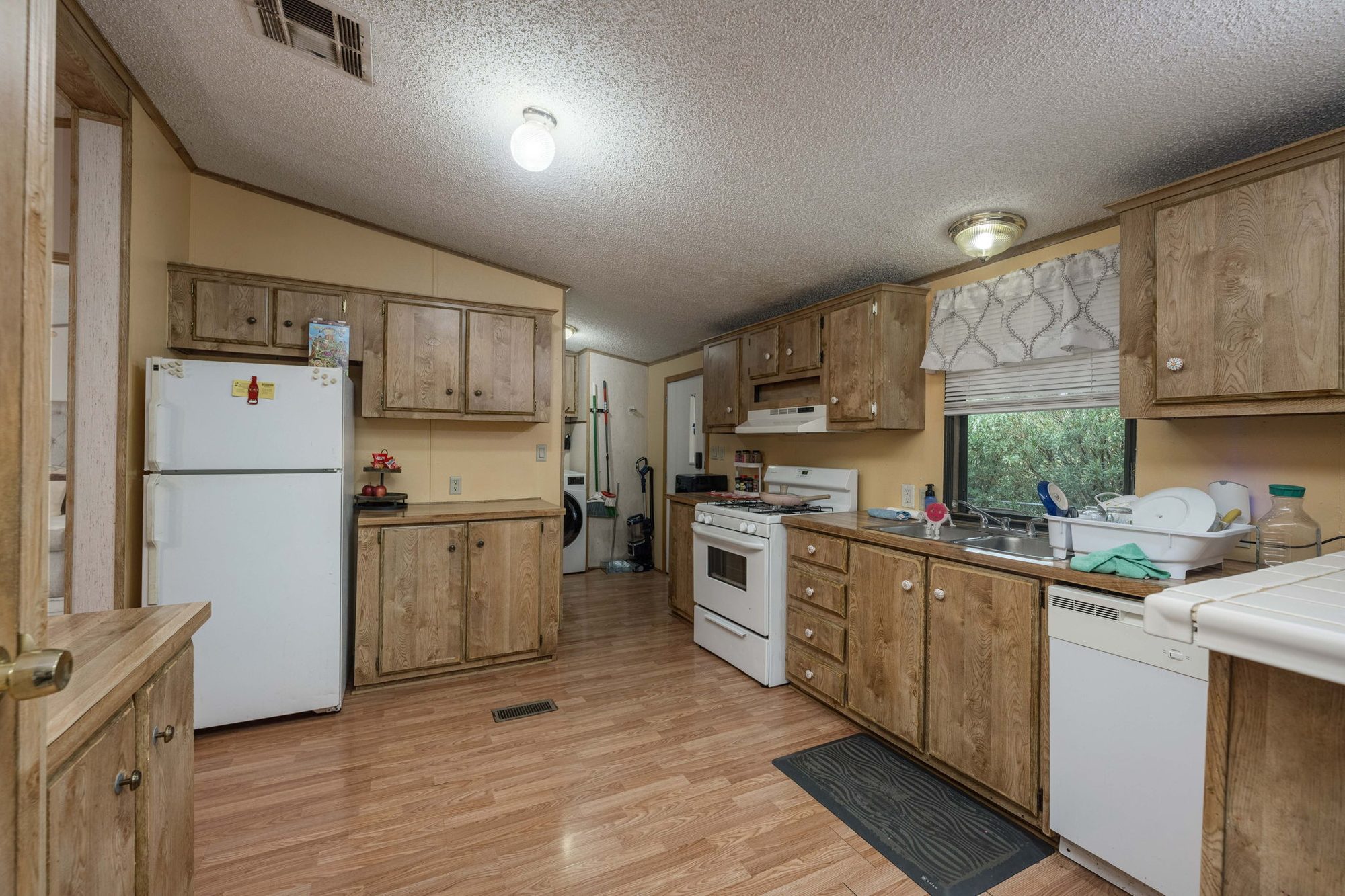 Kitchen with wood cabinetry, gas range, dishwasher, and window over the sink