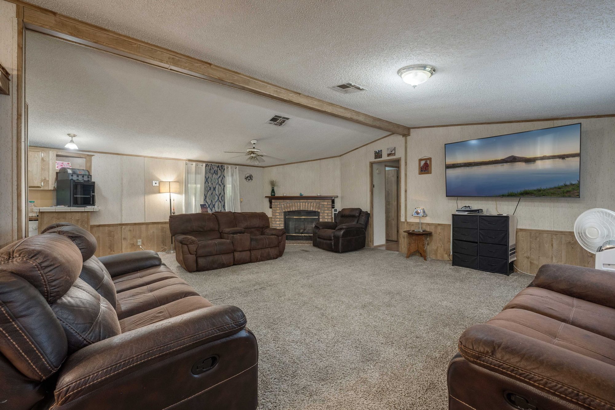 Open living room with a corner brick fireplace, wood wainscoting, and ceiling fan
